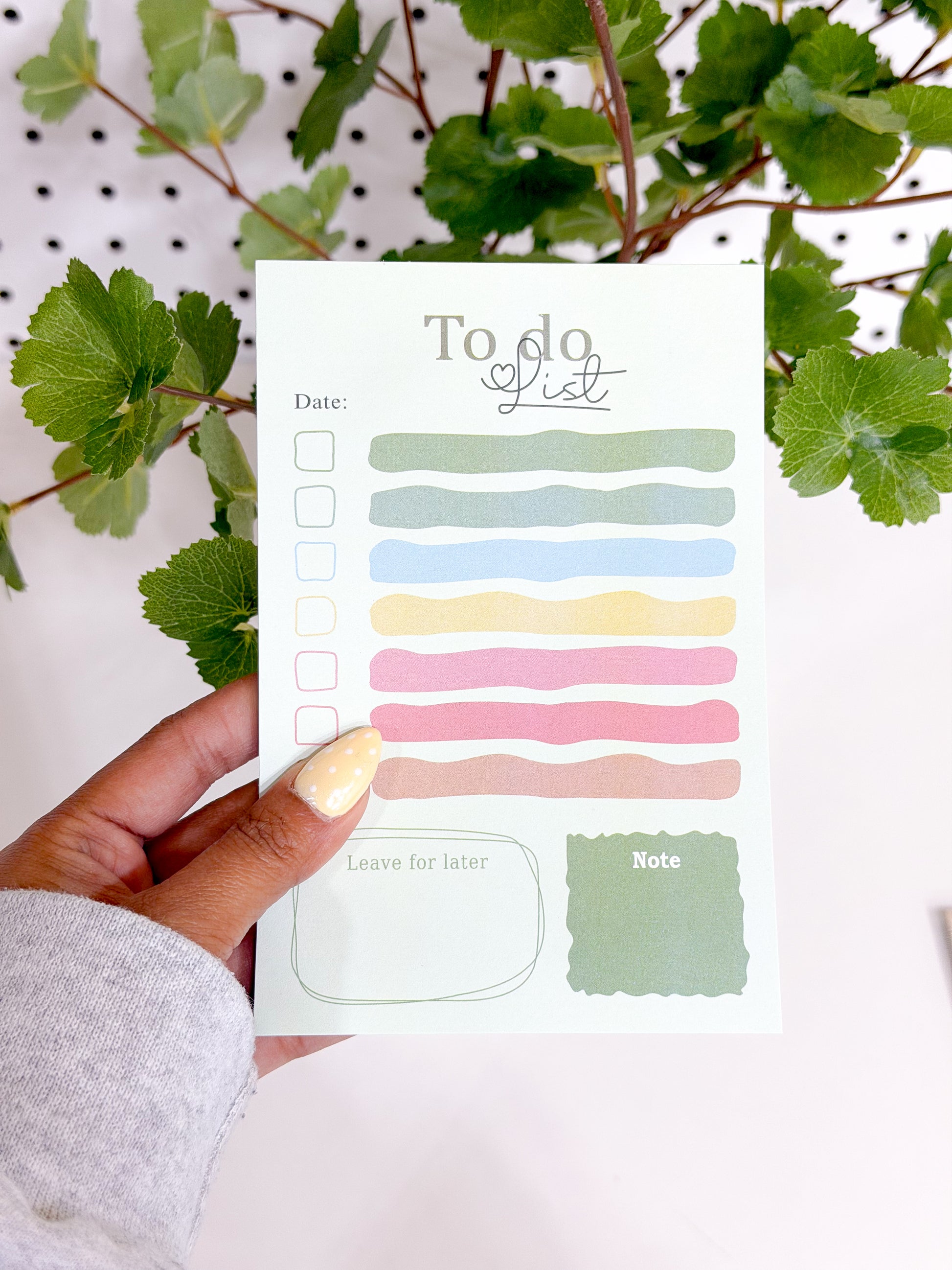 Light green To Do List Notepad with a 'To do list' heading, multi-colored task lines, and checkboxes, held by a hand with dotted yellow nails.
