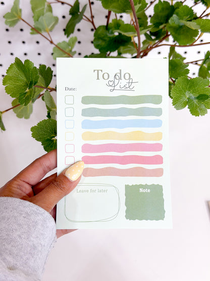 Light green To Do List Notepad with a 'To do list' heading, multi-colored task lines, and checkboxes, held by a hand with dotted yellow nails.
