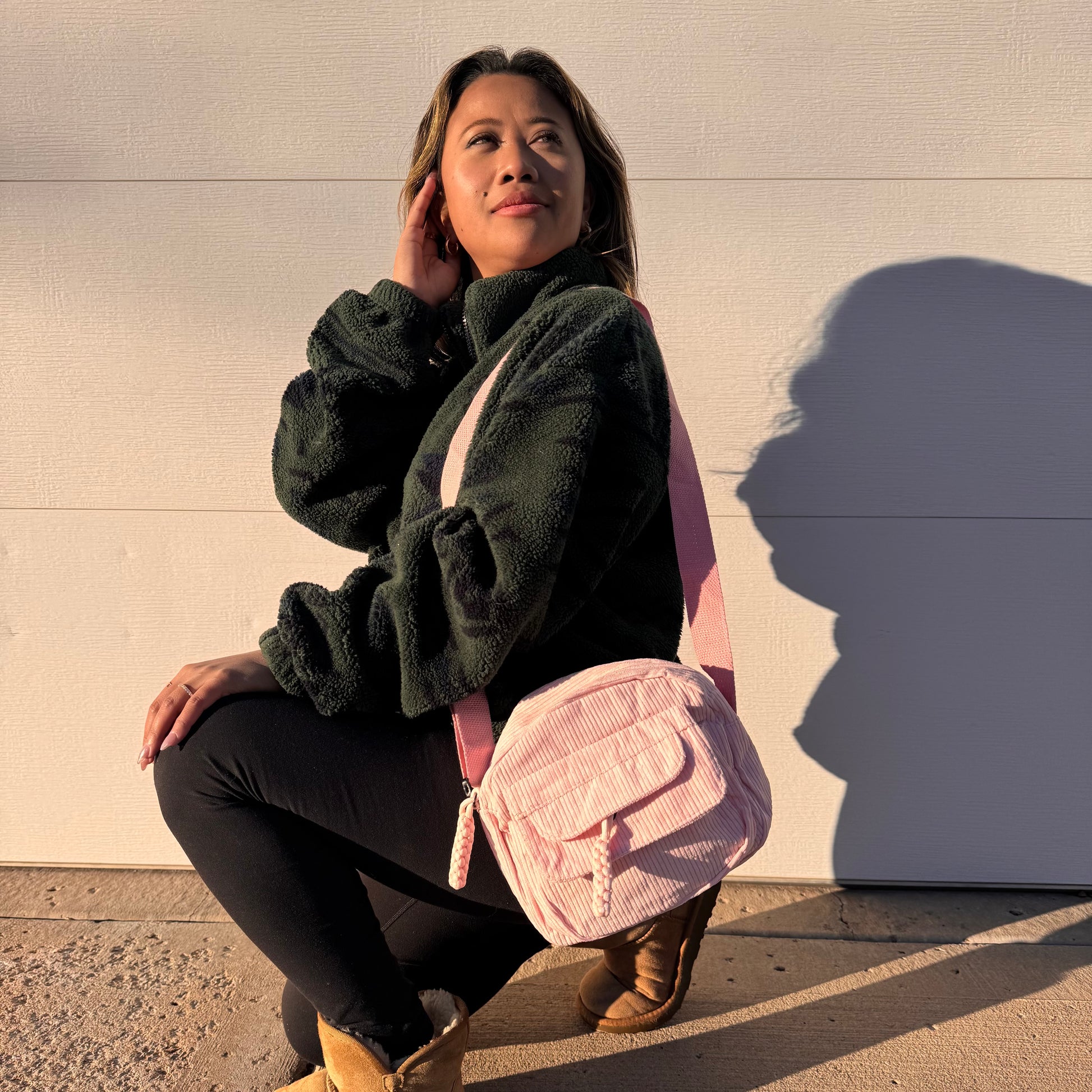 Pink corduroy crossbody bag from Free People, styled with a matching strap and worn with an olive green fleece jacket.