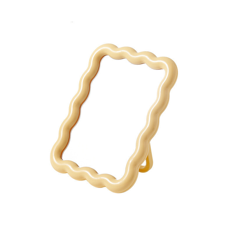 Pale yellow mirror with a wavy, rippled frame, standing upright with a kickstand.