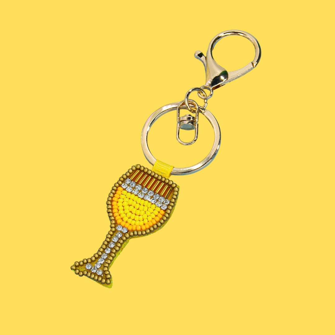 Yellow and gold beaded martini glass bag charm with white rhinestones and a shiny gold clasp, angled on a yellow background.
