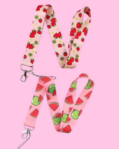 Two pink phone lanyards, one patterned with red strawberries and green flowers, the other with watermelons and slices, both with metal clasps.