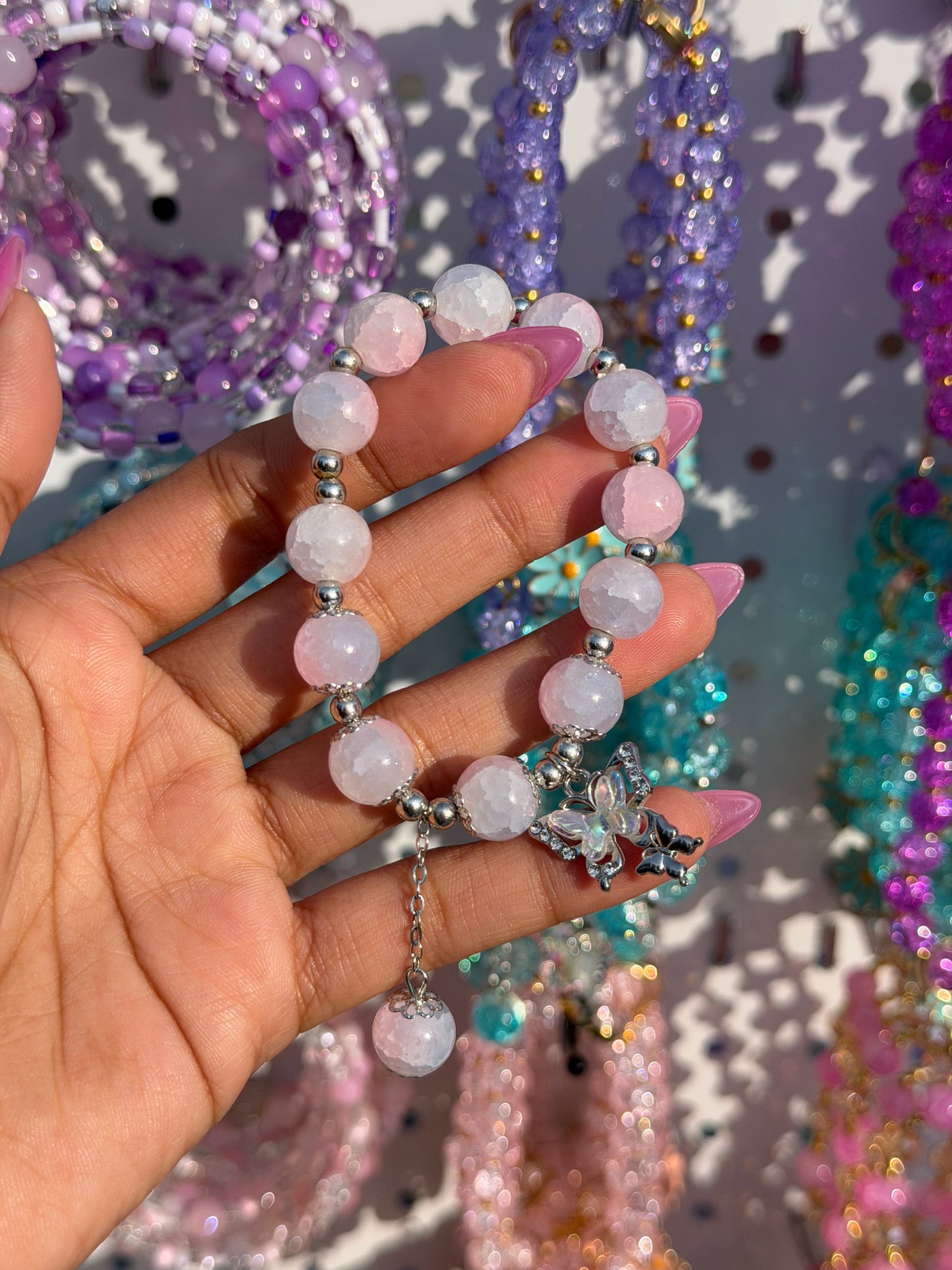 Light pink and white cracked bead bracelet with a sparkling monarch butterfly charm, held by a hand with pink nails.