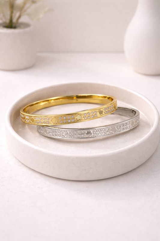 Gold and silver paved bangle bracelets with daisy patterns, displayed on a cream tray.