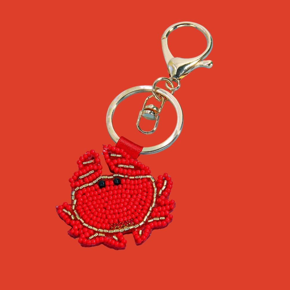Red and gold beaded crab bag charm with black eyes, attached to a gold-tone keyring and clasp.