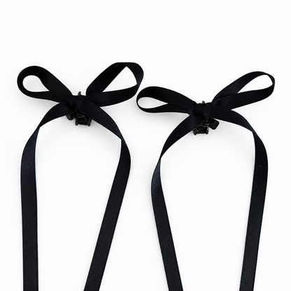 A set of two black bow mini hair clips with long satin ribbons on a white background.