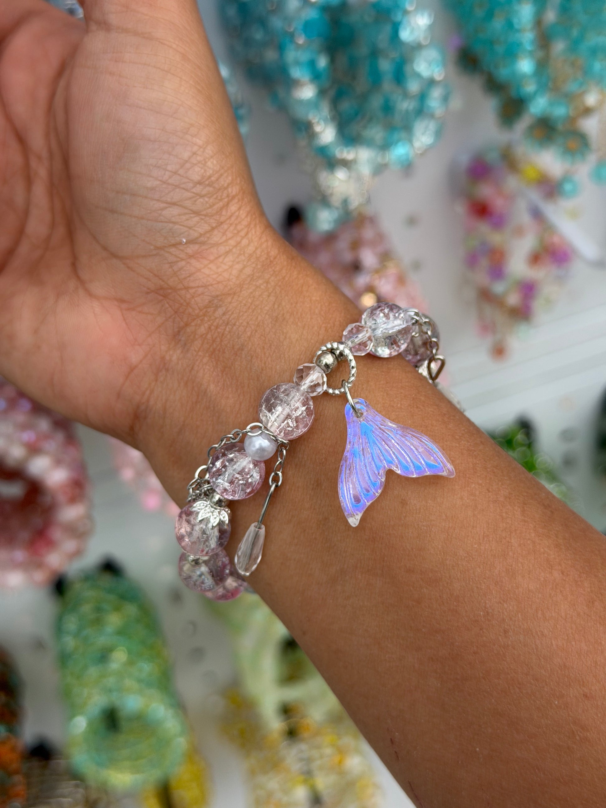 Mermaid beaded bracelet with pink and clear beads and an iridescent purple mermaid tail charm on a person's wrist.