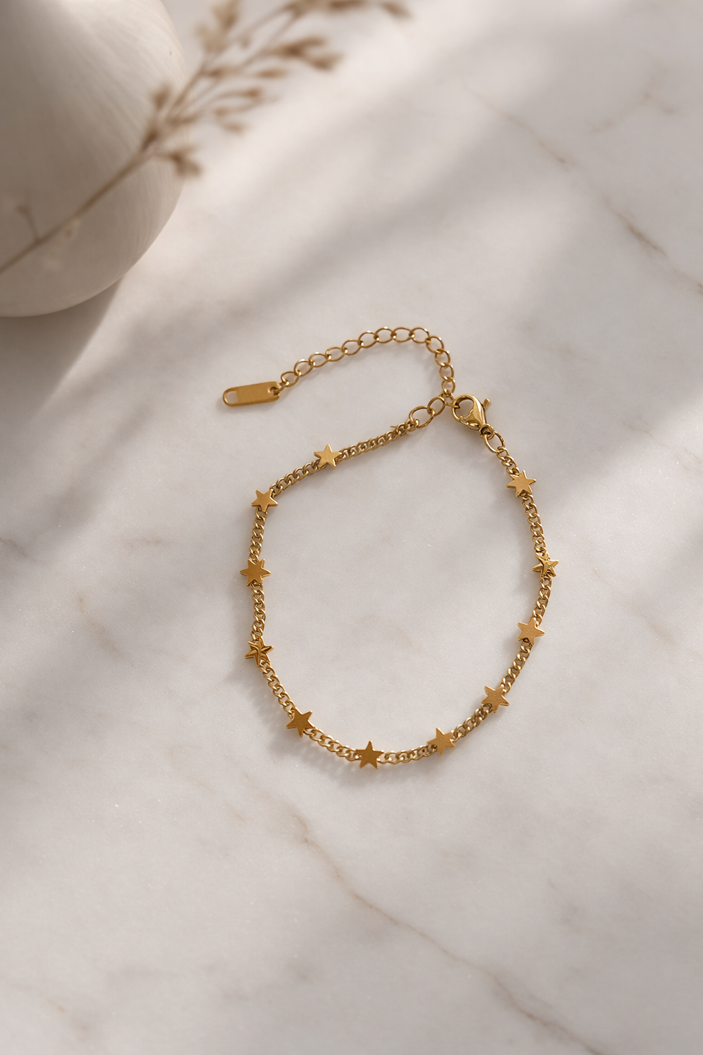 Gold metal chain bracelet with evenly spaced star charms, resting on a white marble surface.