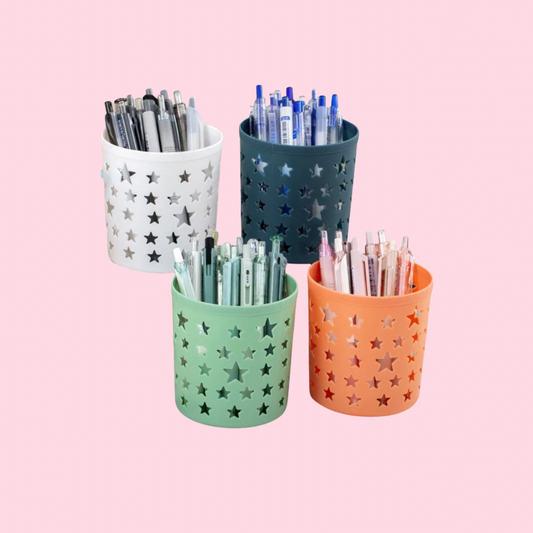 Single pastel plastic desk pen holder with star-shaped cutout design. Shown with pens for display purposes only; pens not included. Available in white, dark teal, mint green, or peach, on a light pink background.