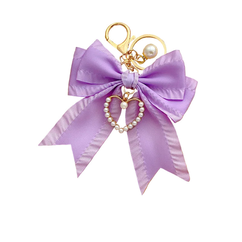 Pearl bow bag charm with a lavender satin bow, gold-tone clasp, and a heart-shaped pearl charm.