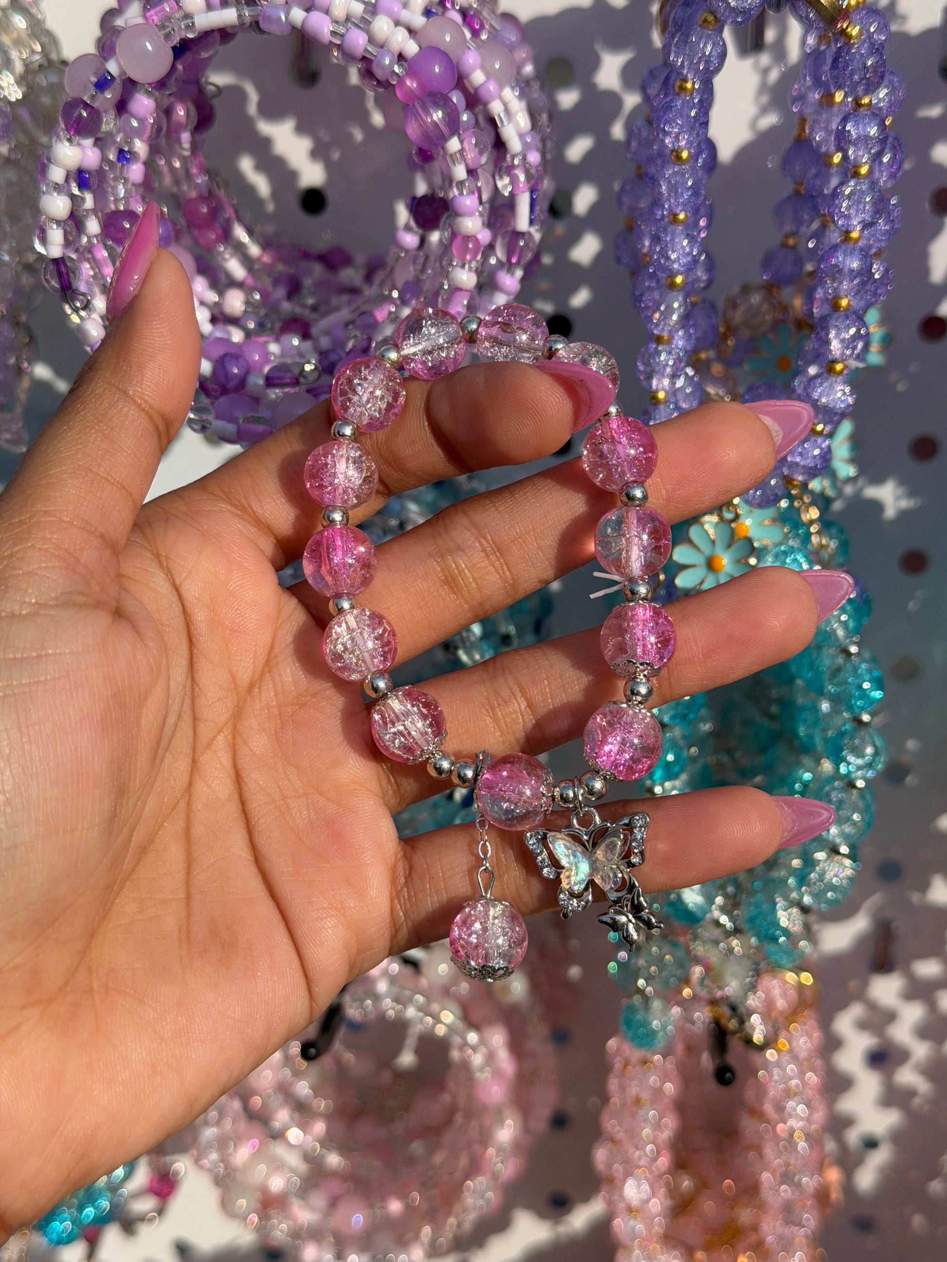 Pink crackle beaded bracelet with a large iridescent butterfly charm and silver accent beads, held by a hand with pink nails.