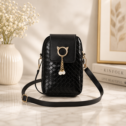 Black woven phone crossbody pouch featuring a gold cat-ear ring and pearl charm, displayed on a marble surface.