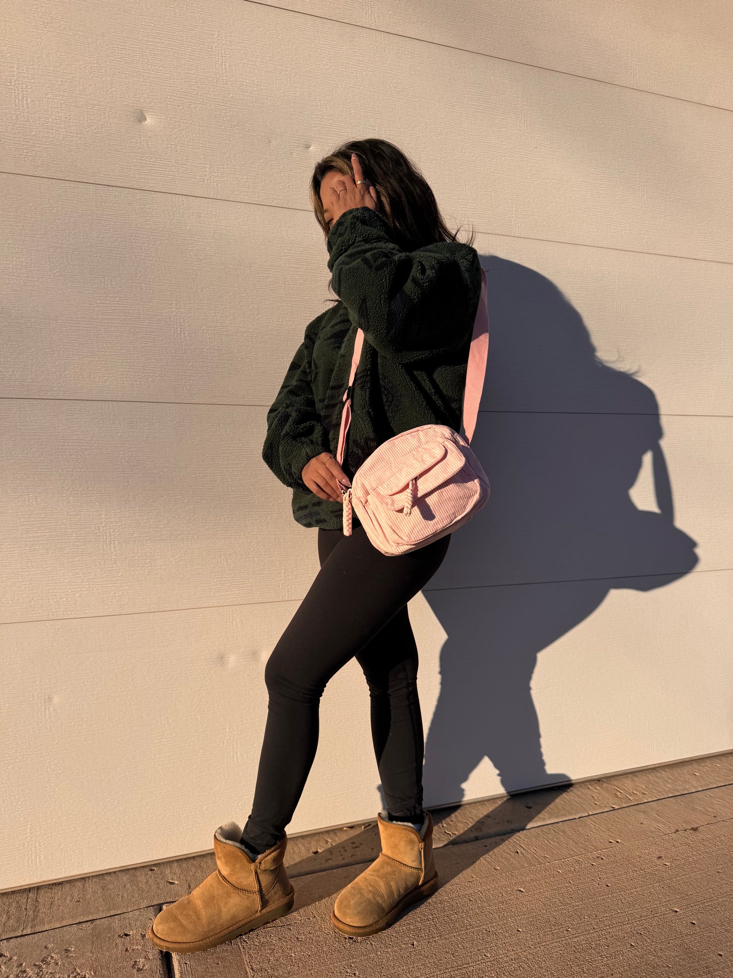 Pink crossbody bag by Baggu with a corduroy texture, styled with a fleece jacket, leggings, and casual boots.