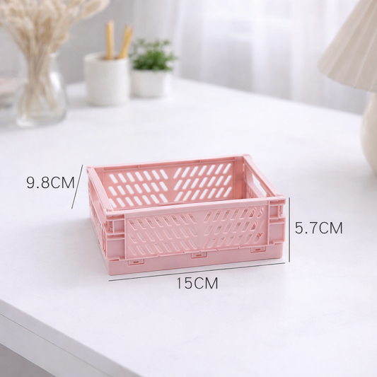 Pink collapsible plastic storage crate with perforated sides, shown open on a white table. The crate folds flat and measures 15 by 9.8 by 5.7 centimeters.
