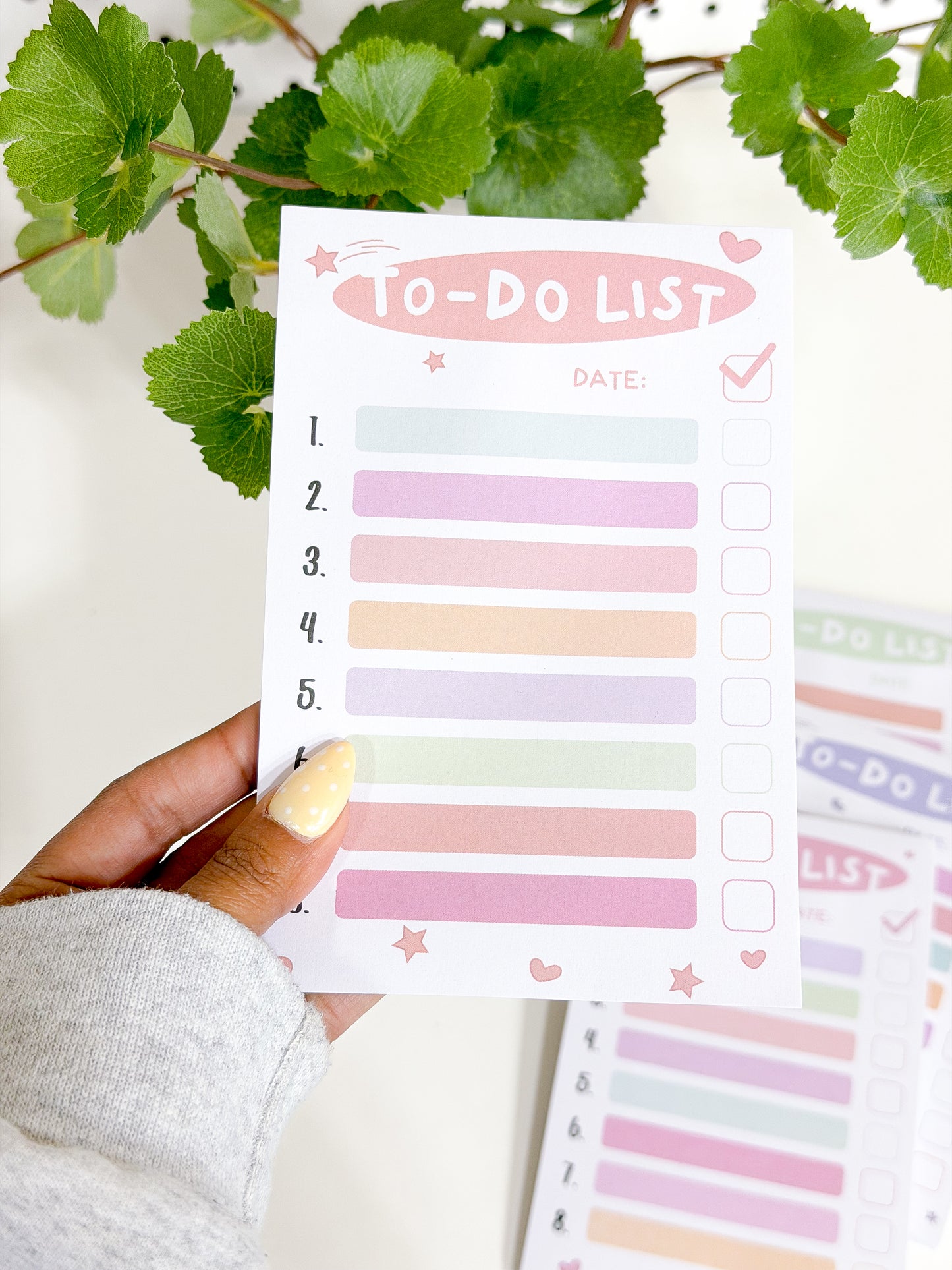 White Tasks Notepad with numbered pastel lines and checkbox squares, decorated with pink stars and hearts, held in a hand.