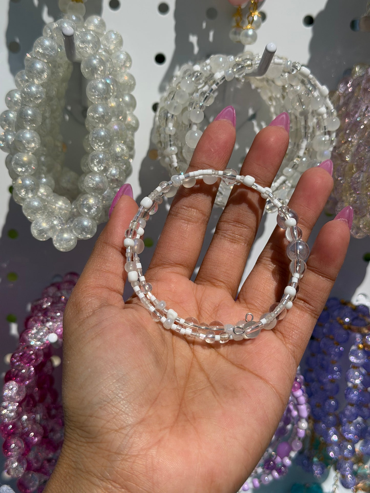 Layered beaded bracelets with white and clear beads held in a hand, featuring multiple delicate strands.