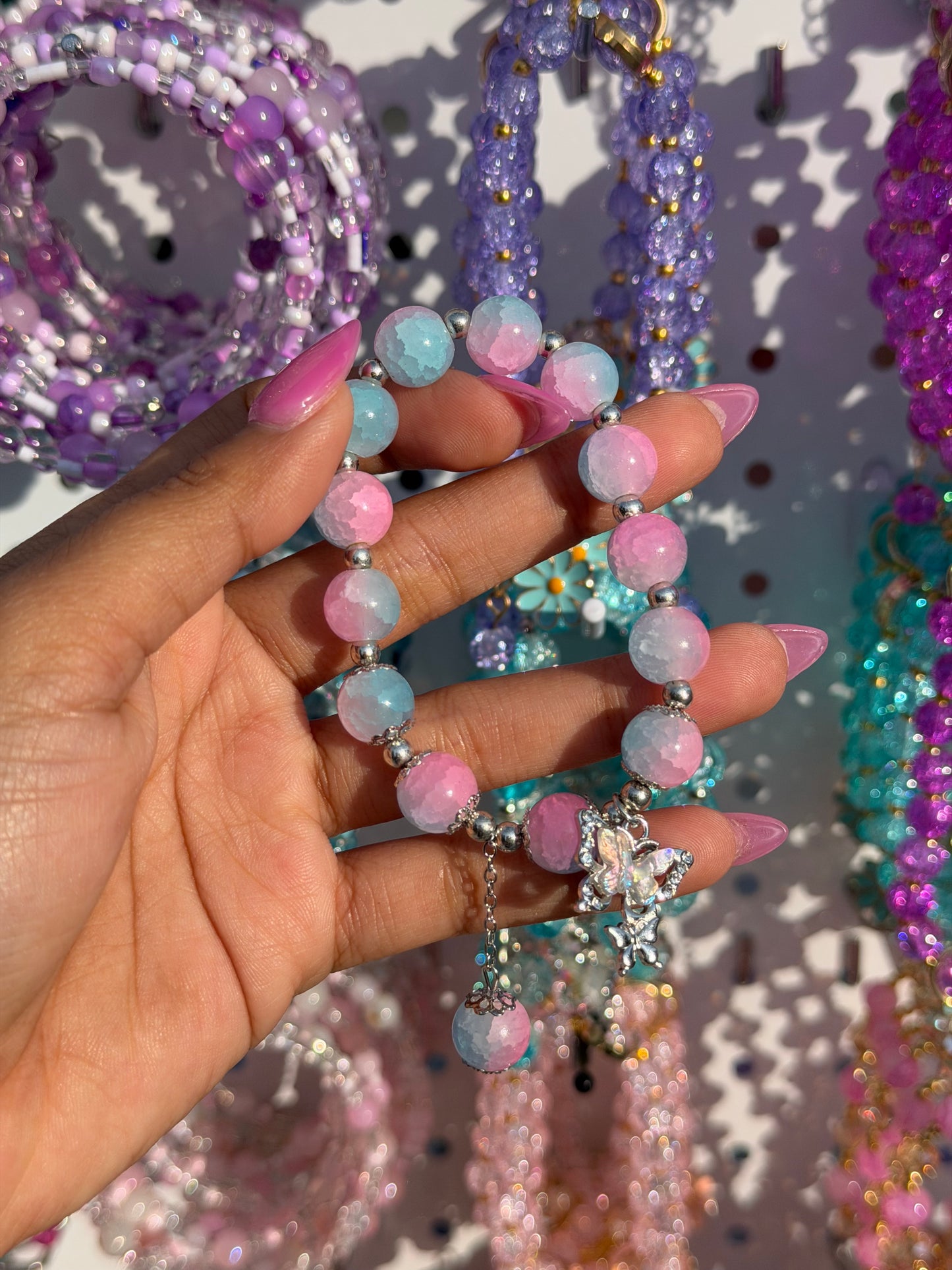 Frosted pink and blue ombre beaded bracelet with a silver butterfly charm, held by a hand with pink nails.