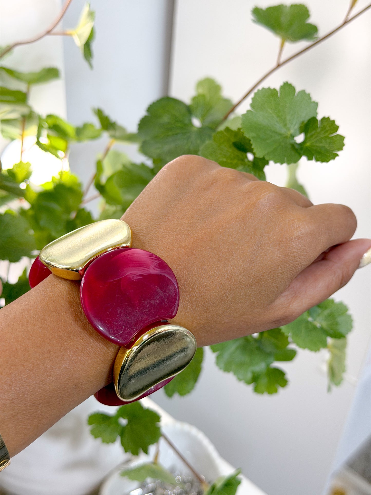 Chunky statement bracelet with fuchsia and gold irregular pieces, worn on a hand with green foliage.