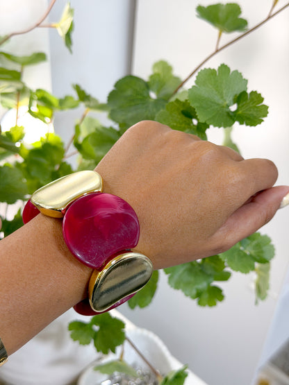 Chunky statement bracelet with fuchsia and gold irregular pieces, worn on a hand with green foliage.