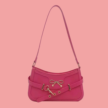 Small hot pink shoulder handbag with bow detail, adjustable strap, and gold-tone hardware, displayed on a pink background.