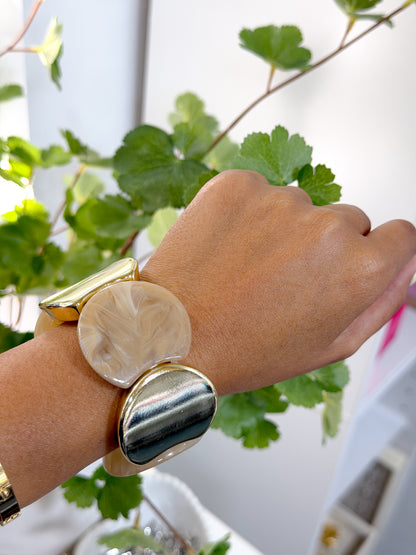 Chunky statement bracelets featuring swirled beige resin and polished gold-tone segments, worn with a gold-tone bangle on a woman's wrist.