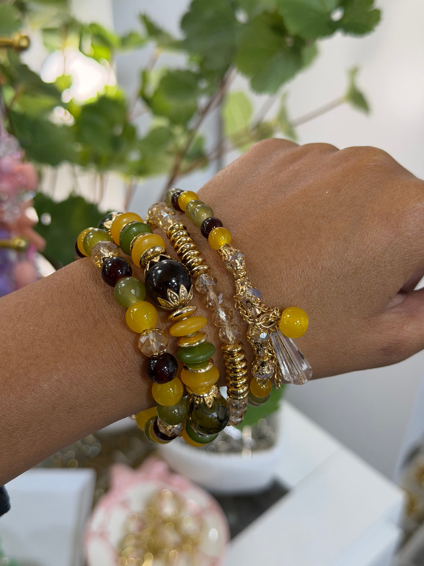 Layered Beaded Charm Bracelets in yellow, green, and brown, with gold accents and clear charms, styled on a person's wrist.