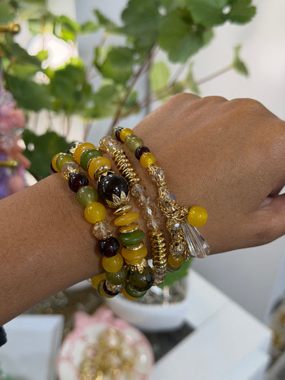 Layered Beaded Charm Bracelets in yellow, green, and brown, with gold accents and clear charms, styled on a person's wrist.