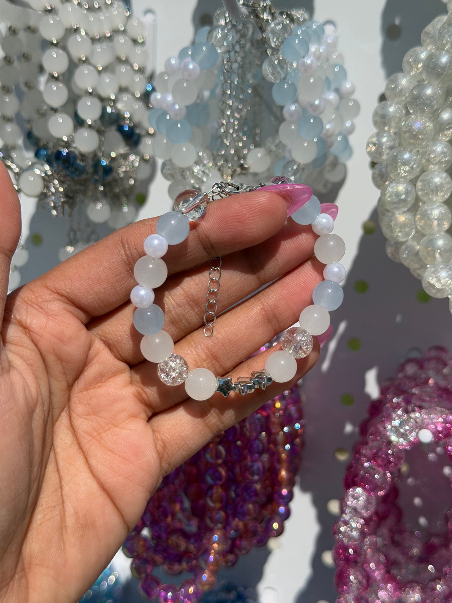 White beaded bracelet with light blue, clear crackle beads and silver star charms, held by a hand.