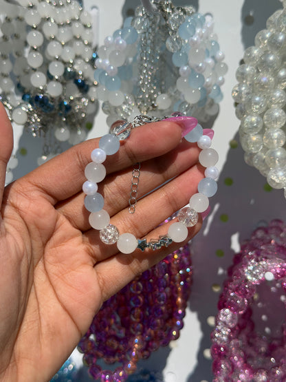 White beaded bracelet with light blue, clear crackle beads and silver star charms, held by a hand.