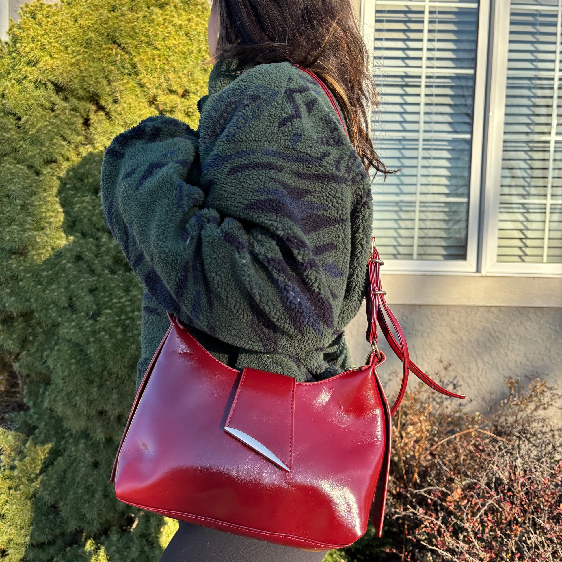 Red shoulder bag by unknown brand with silver detail on the flap, worn with a fuzzy green jacket.