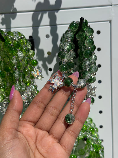 Green and clear crackle glass beaded bracelets with silver accents, a butterfly charm, and an extender chain, held in a hand with pink nails.