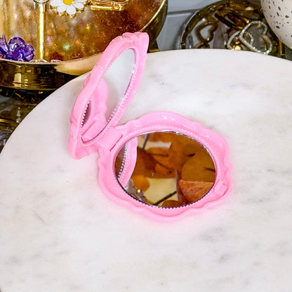 Pink rose compact mirror from unknown vendor, displayed open on a white marble surface.
