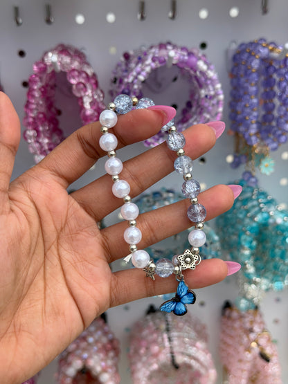 Butterfly Pearl Beaded Bracelet with white pearls, clear cracked beads, and silver accents, featuring a blue butterfly, flower, and starfish charm, held by a hand.