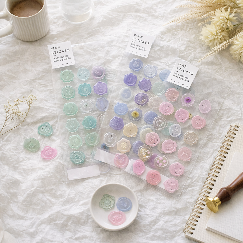 Wax seal stickers by ZAOMO with floral designs in pastel shades, displayed on crinkled fabric with a cup and notebook.