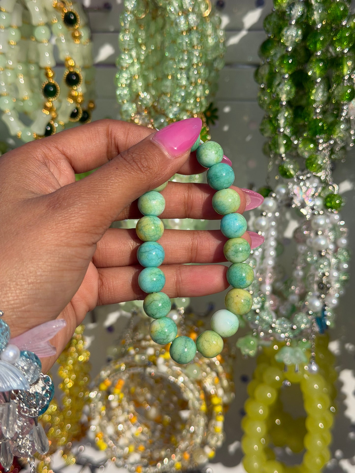 Green marble beaded bracelet with varied green and turquoise cracked beads, held by a hand with pink nails.