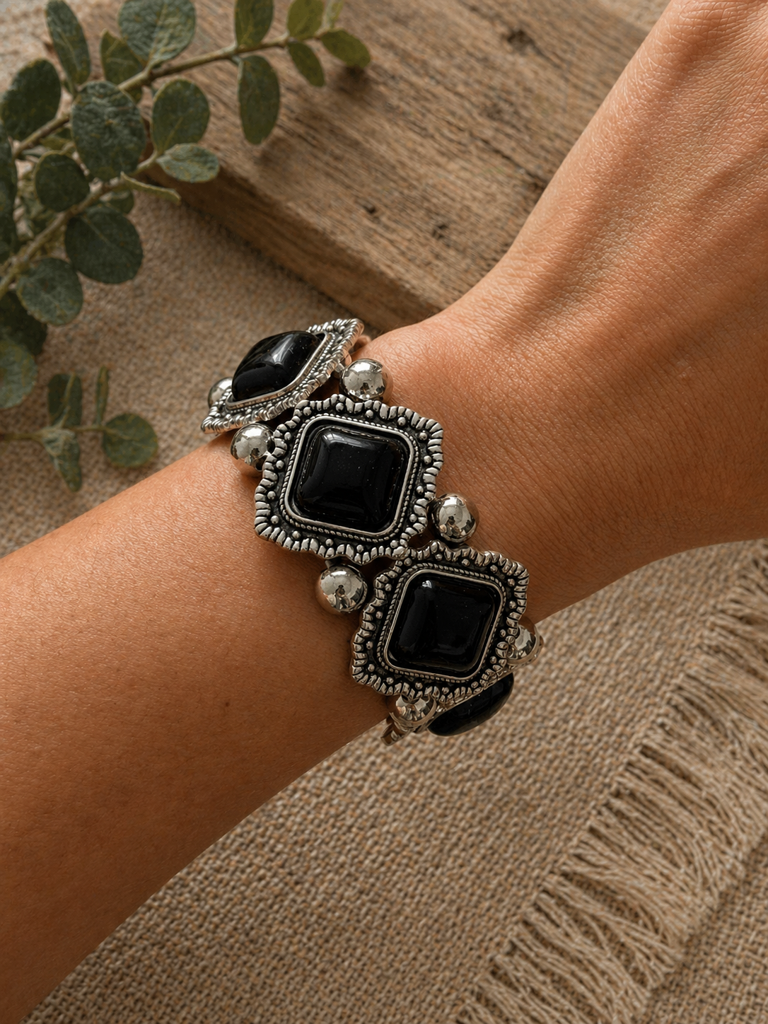 Chunky bracelet featuring black rectangular stones set in ornate silver-toned metal, worn on a wrist.