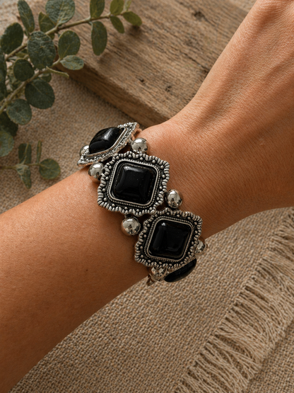 Chunky bracelet featuring black rectangular stones set in ornate silver-toned metal, worn on a wrist.