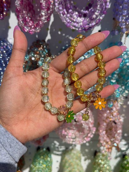 Yellow and clear beaded daisy bracelets held in a hand with pink nails.