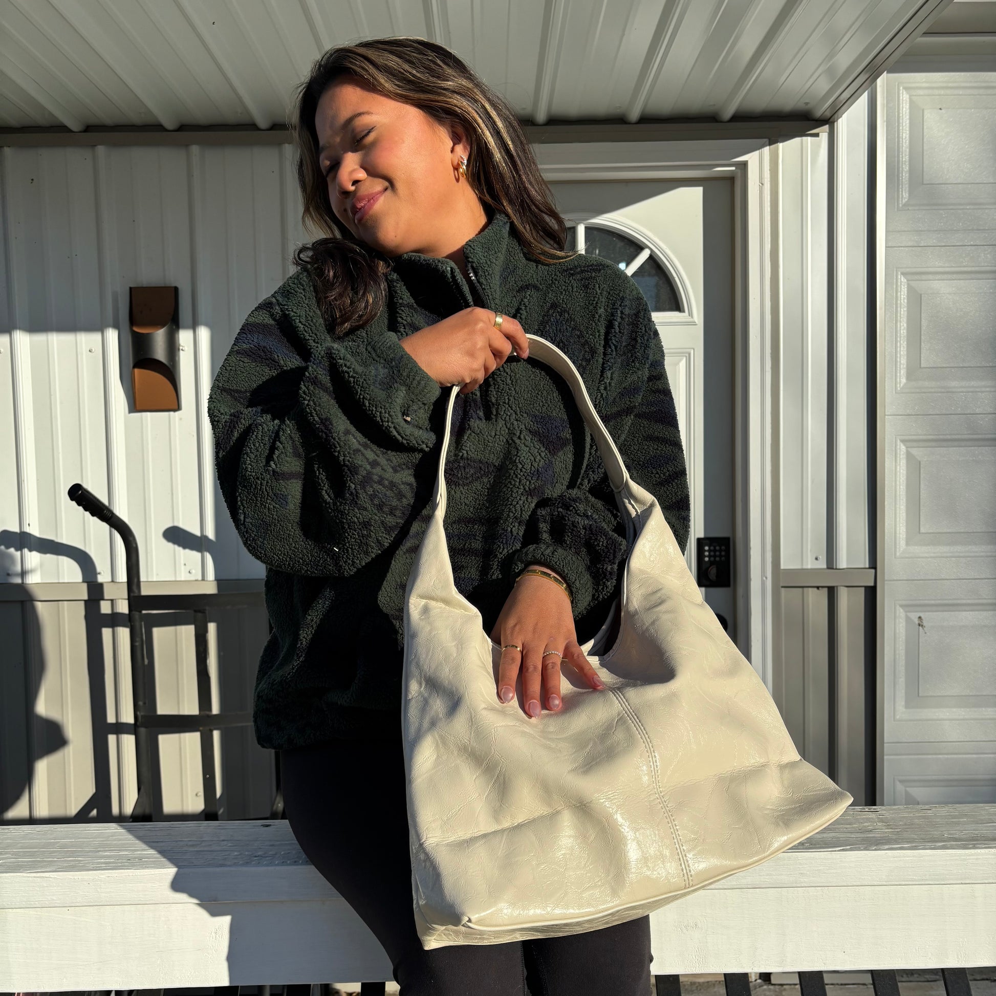 Beige faux leather tote bag with soft creases, by The Downtown Tote Bag, held by a person wearing a dark fleece jacket, gold jewelry, and leggings.