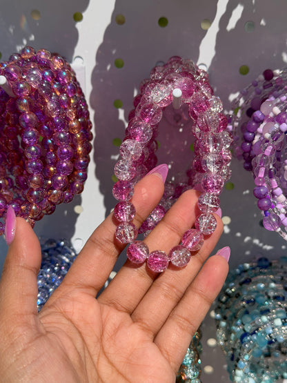 Pink Beaded Bracelets with cracked glass texture, held by a hand with pink nails, alongside purple and blue bracelets.