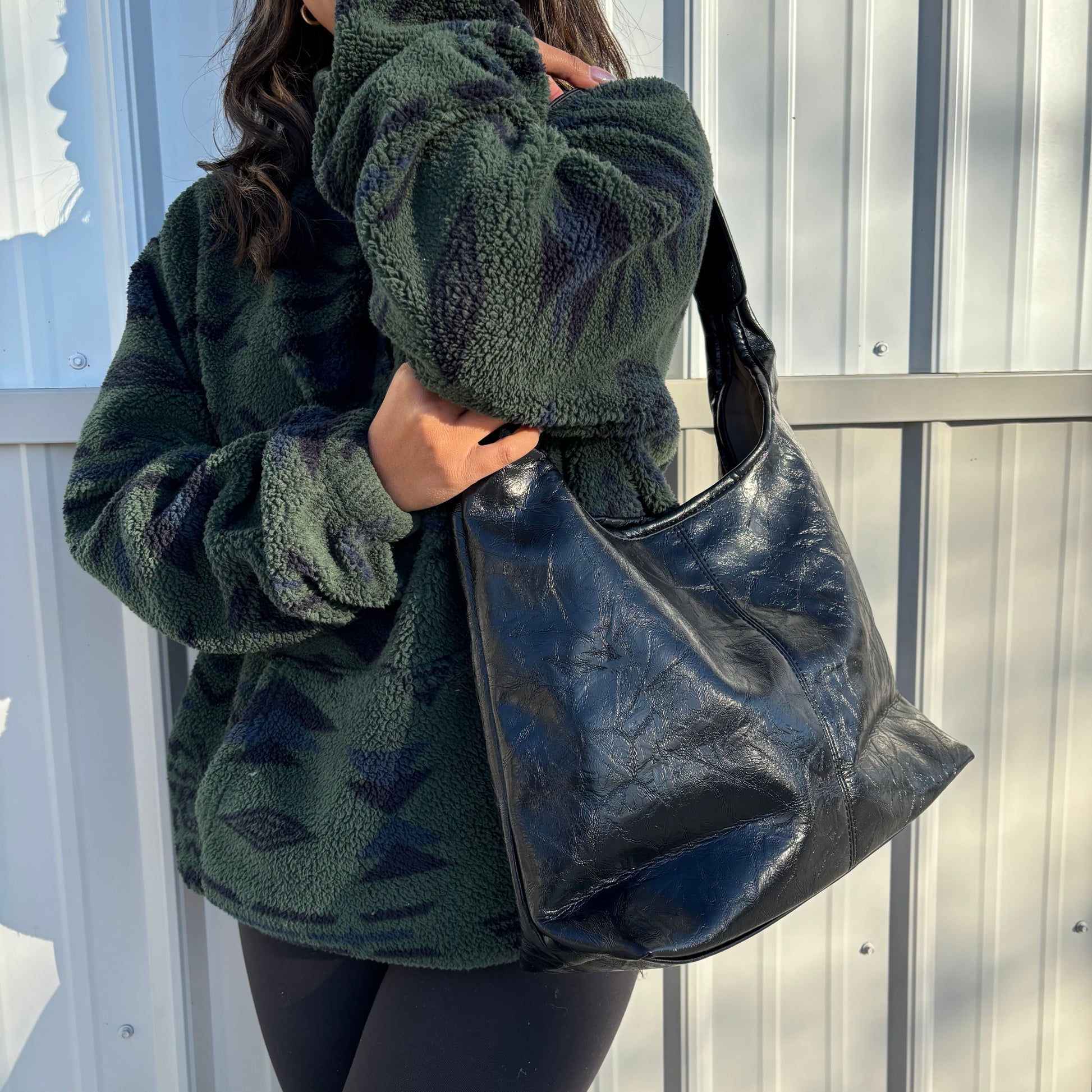 Black leather tote bag with shoulder strap, styled with a green patterned fleece jacket and black leggings.