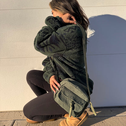 Green corduroy crossbody bag by BAGGU, styled with a fleece jacket, black leggings and brown UGG boots.
