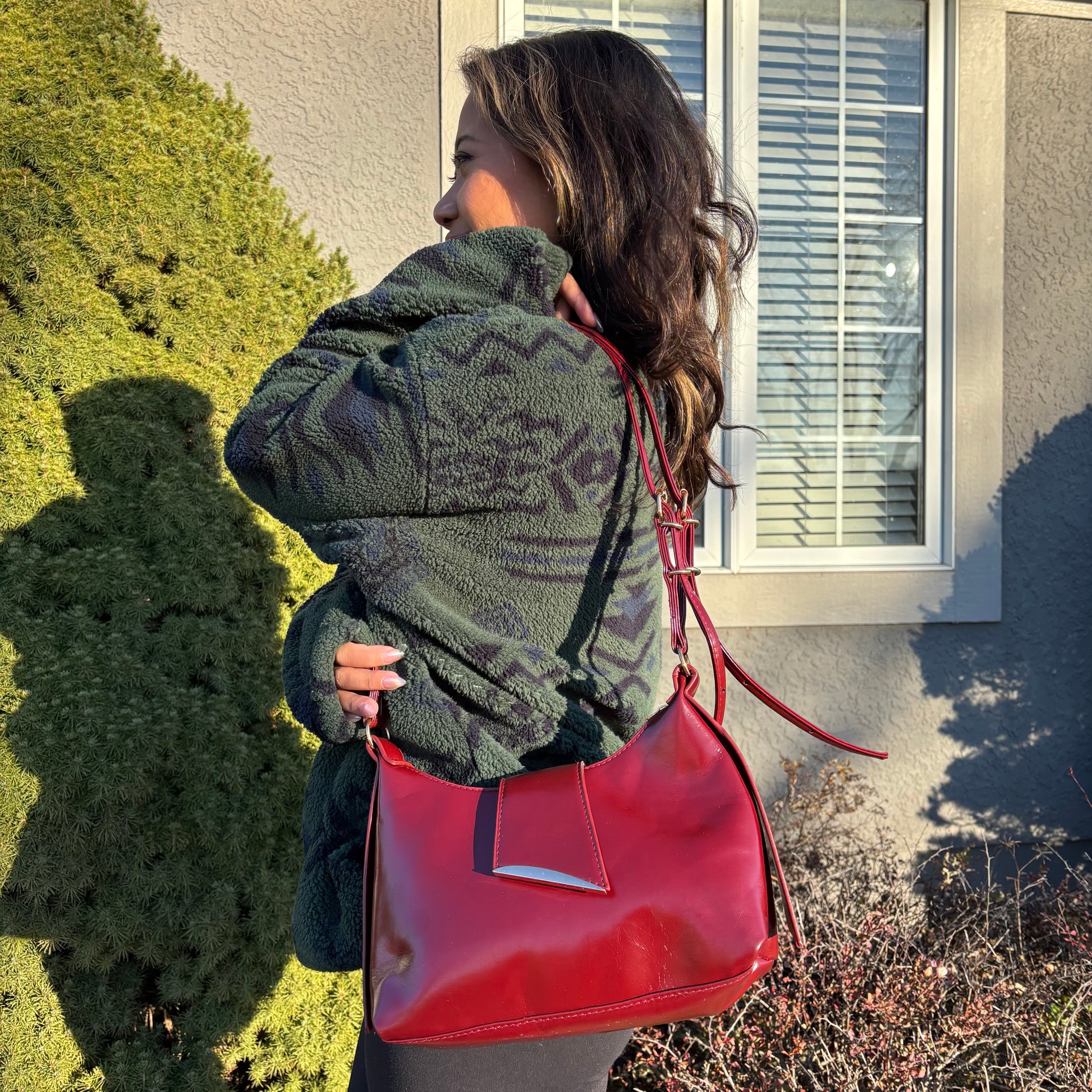 Red leather shoulder bag by unknown brand with a silver accent, worn with a patterned fleece jacket.