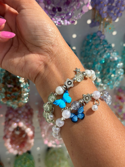Butterfly Pearl Beaded Bracelet with white pearls, blue butterfly, flower and star charms, and cracked glass beads, worn on a wrist.