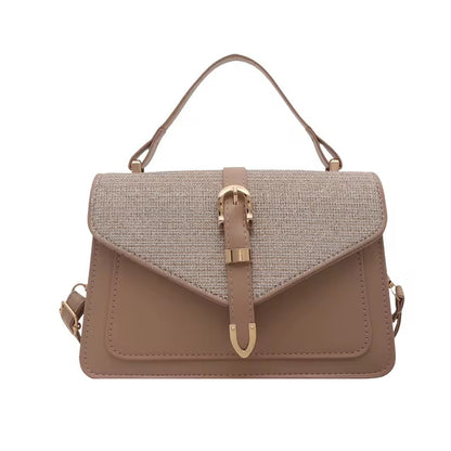 Taupe flap bag with buckle detail from The Uptown, featuring a woven top flap and shoulder strap.