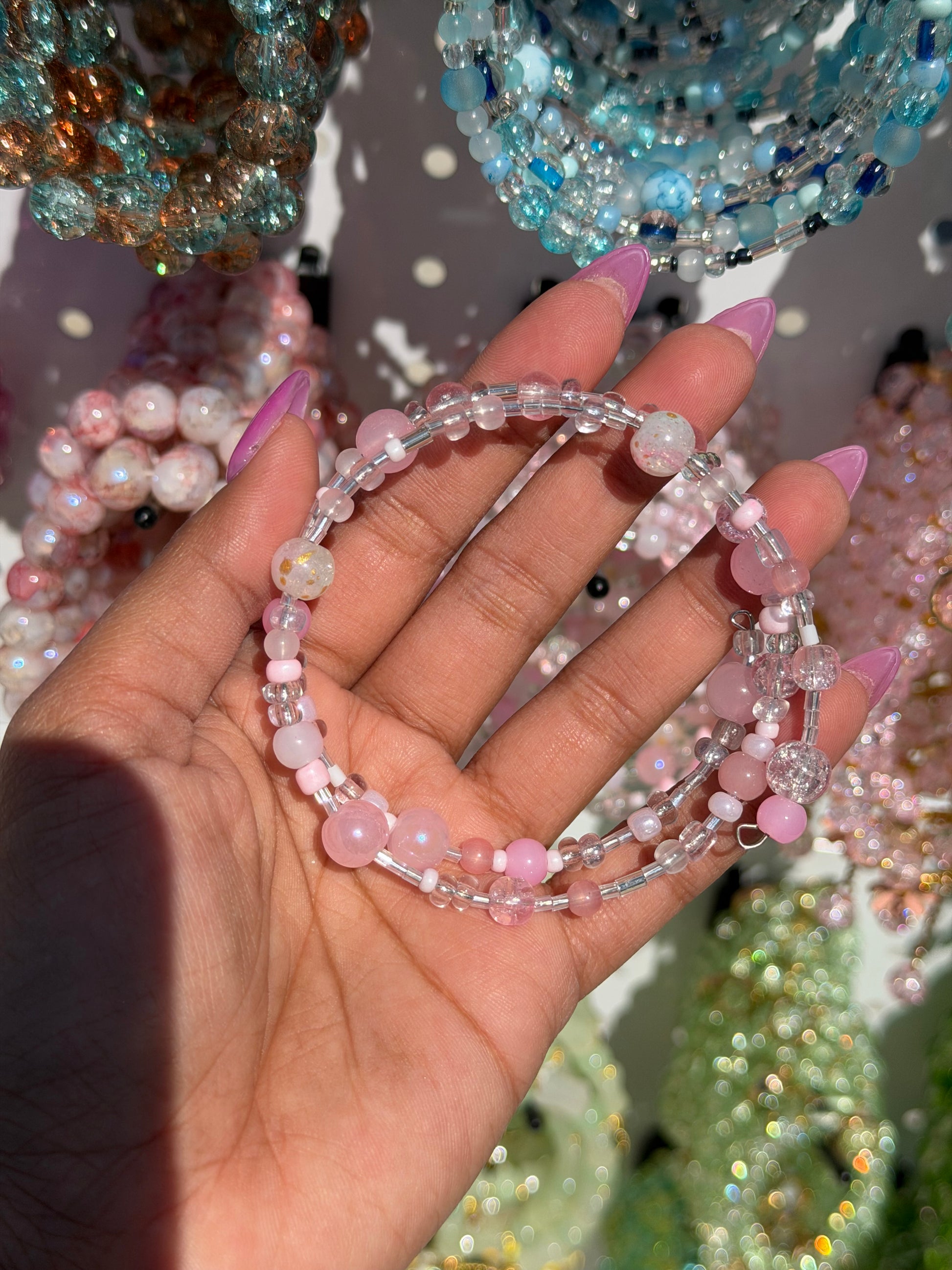 Layered beaded bracelets in pink and clear, featuring various bead textures, held by a hand with pink nails.