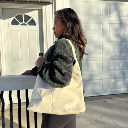 Ivory tote bag from an unknown brand, with a wrinkled texture and carried by a woman wearing a green, camouflage fleece jacket.