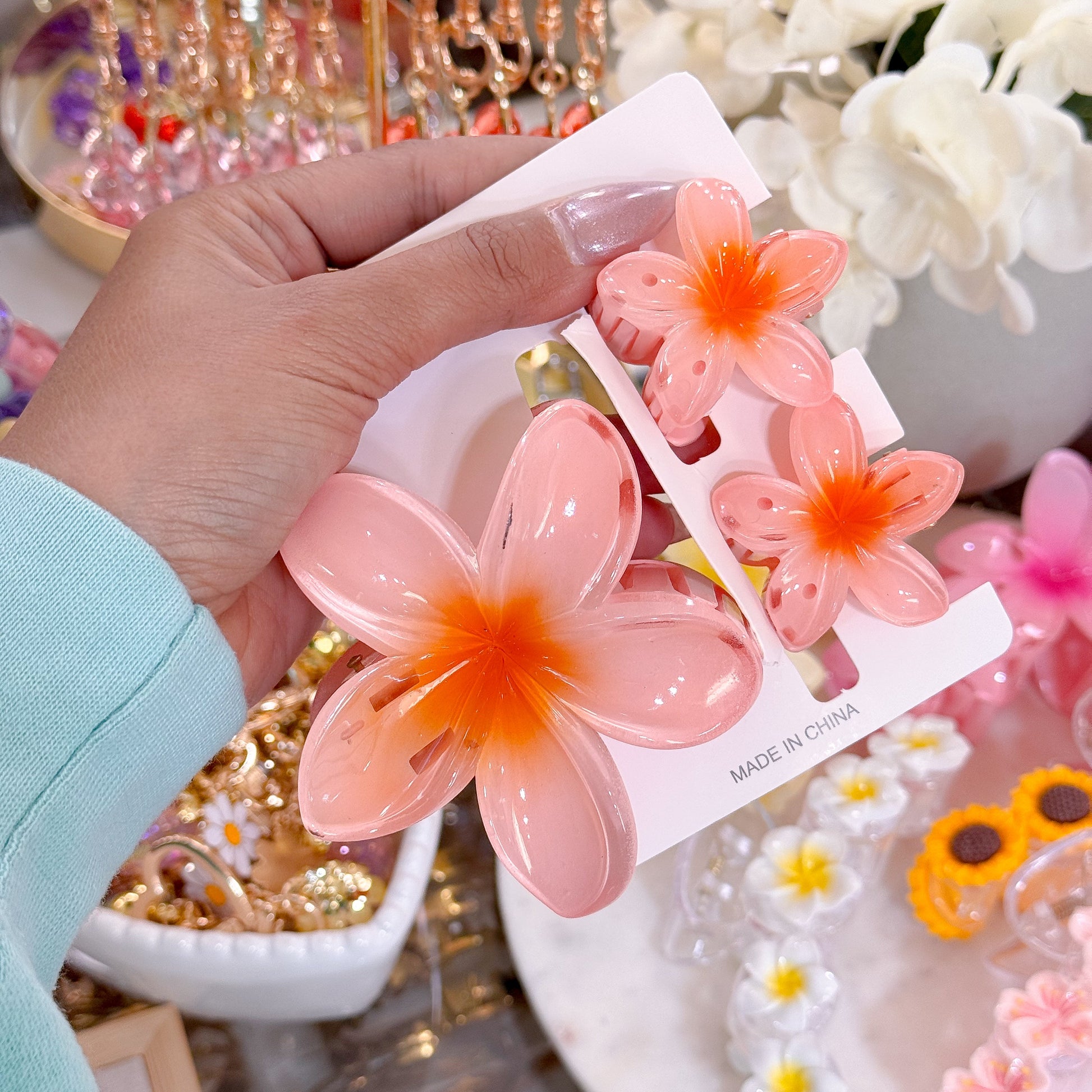 Orange plumeria hair clip sets with floral accents, presented on white cardboard, reading "Made in China".