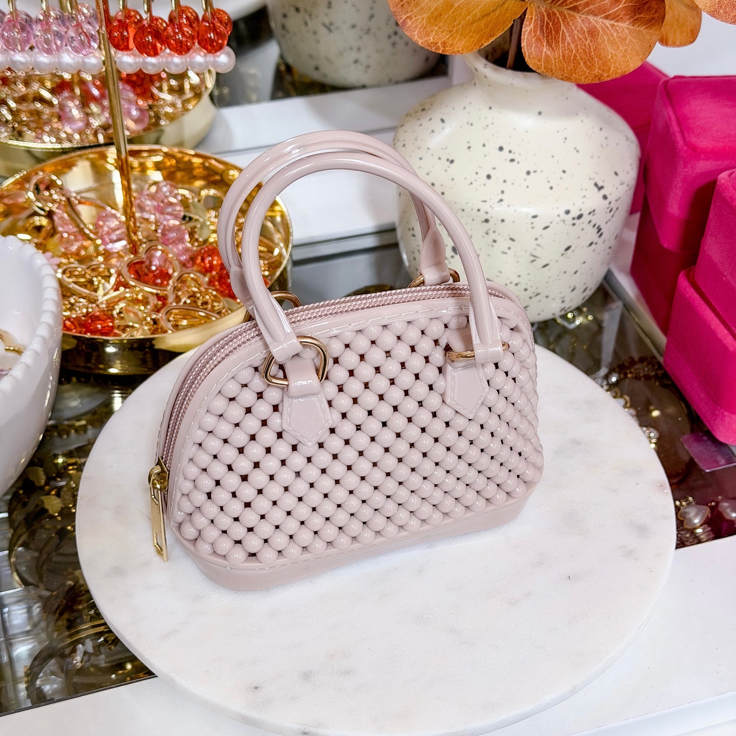 Pale pink mini dome bag with beaded texture, from an unknown brand, sitting on a marble platform.
