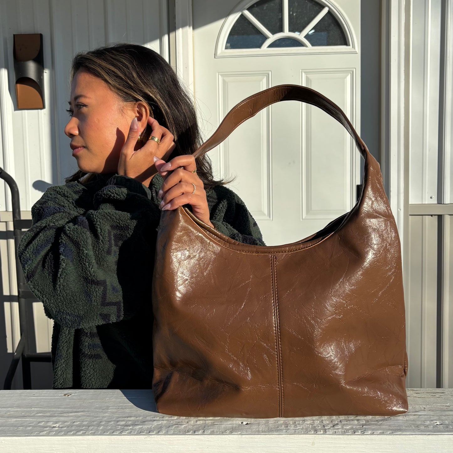 Brown leather tote bag with top handle by Hobo, shown with a model wearing an olive green patterned fleece jacket.
